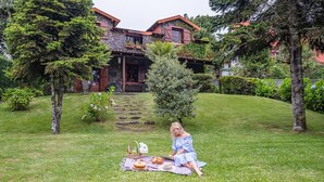 A person sitting on a blanket in a grassy area with a house in the background. - Villa Achada da Mouca by Homie (Santana)