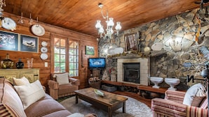 A cozy log cabin interior with a stone fireplace, wooden furniture, and a television. - Villa Achada da Mouca by Homie (Santana)