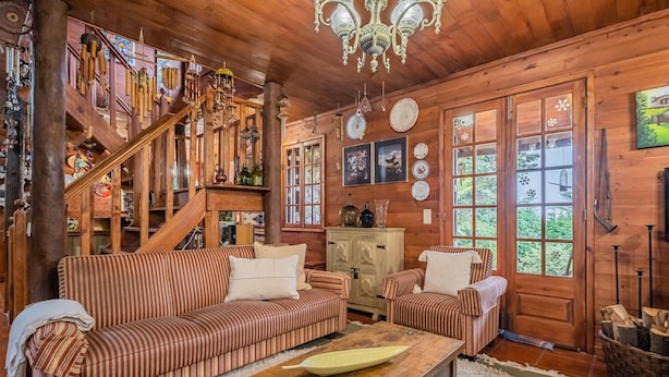 A cozy cabin interior with a striped sofa, a wooden coffee table, and a staircase with hanging decorations. - Villa Achada da Mouca by Homie (Santana)