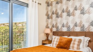A bedroom with a large window, a bed with a brown headboard, and a nightstand with a lamp. - Ocean Panorama Apartment 2 by Homie (Calheta)