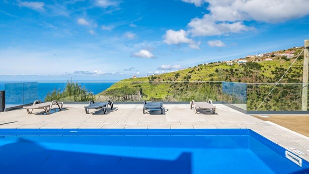 A pool area with lounge chairs and a view of the sea and hills. - Ocean Panorama Apartment 2 by Homie (Calheta)
