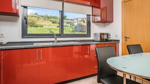 A modern kitchen with red cabinets, a large window, and a dining table with chairs. - Canhas Residence II by Homie (Ponta do Sol)