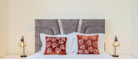 A neatly made bed with a grey headboard, two red pillows with white leaf patterns, and two bedside lamps on either side.