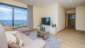 A modern living room with a large window, a sofa, a glass coffee table, and a TV. - Canhas Residence II by Homie (Ponta do Sol)