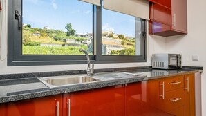 A kitchen with a large window, stainless steel sink, and red cabinets. - Canhas Residence II by Homie (Ponta do Sol)