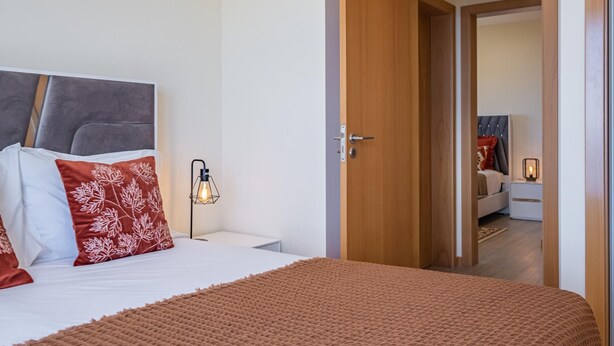 A bedroom with a bed, a nightstand, a lamp, and a wooden door leading to another room. - Canhas Residence II by Homie (Ponta do Sol)