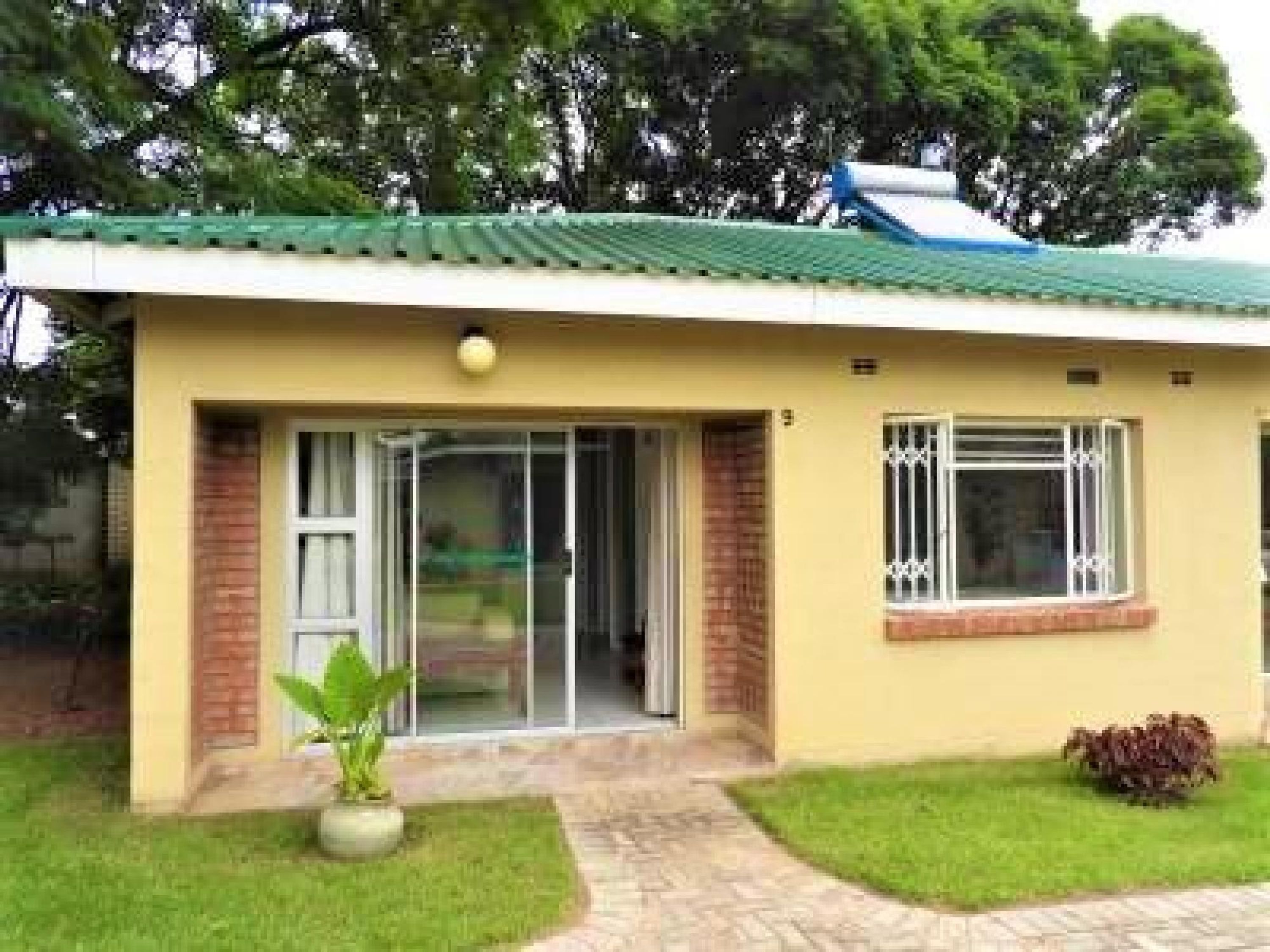 A single-story house with a green roof, a sliding glass door, and a small window with decorative bars.
