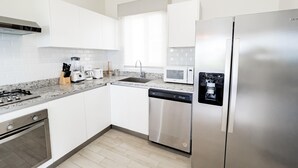 Una cucina moderna con mobili bianchi, elettrodomestici in acciaio inossidabile, un piano di lavoro in granito e una lavastoviglie.