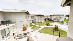 Ein Balkon mit Tisch und Stühlen, ein kleiner Garten und ein Poolbereich.