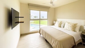 Ein Schlafzimmer mit Bett, Deckenventilator, am Wand befestigtem Fernseher und Fenster mit Blick auf einen Pool.