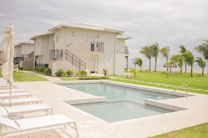 Un área de piscina con sillones de descanso y un edificio que tiene una escalera y un balcón.
