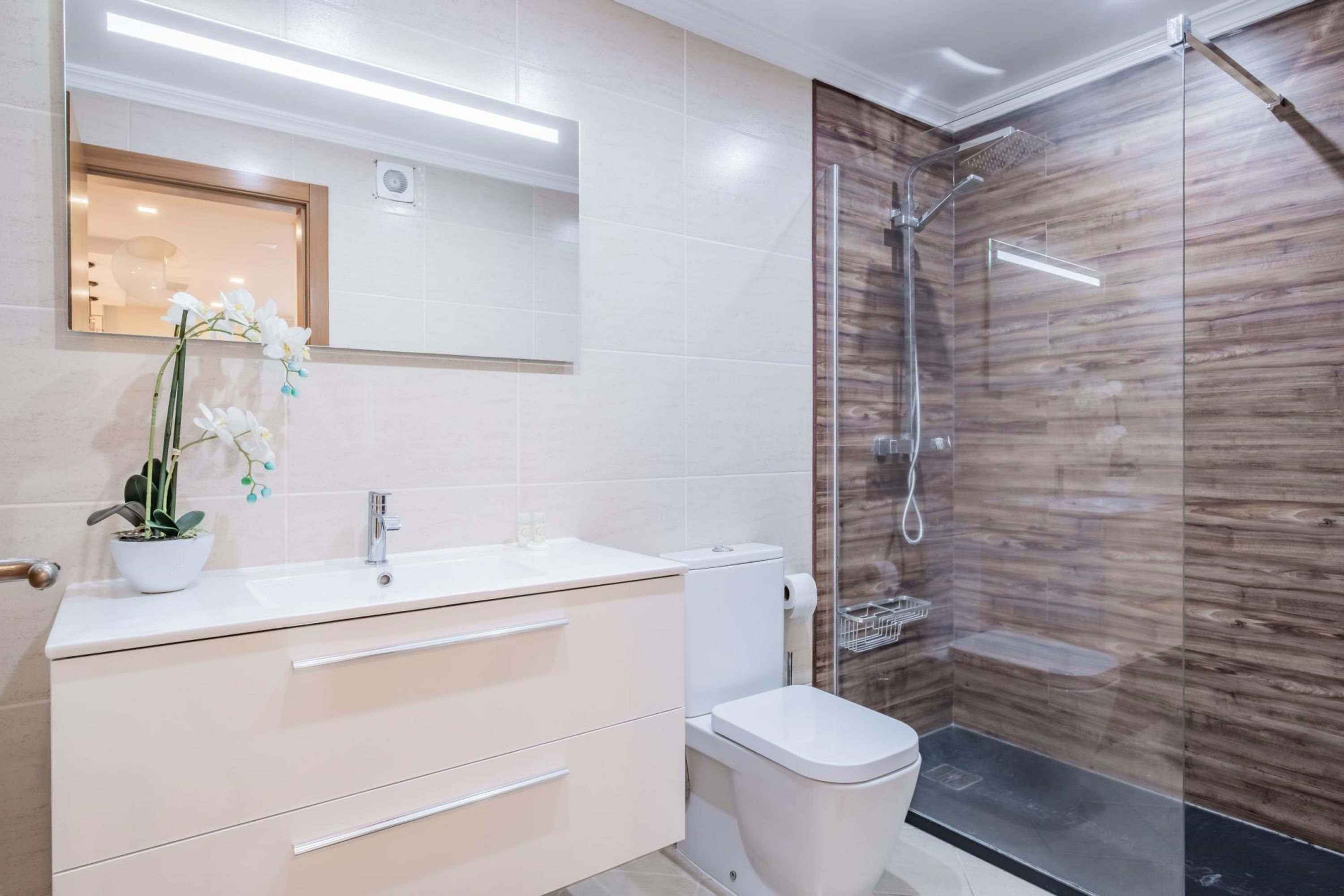 Een moderne badkamer met een witte wastafel, toilet en een douchecabine met glazen wanden.