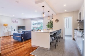 Een modern appartement met keuken, eethoek en woonkamer. Het heeft een groot raam, een bank, een televisie en een eettafel met stoelen.