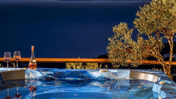 A hot tub with a view of the sea and mountains, two wine glasses, and a bottle of wine on a table. - Elena Junior Deluxe Suite by Estia (Agios Vasileios)