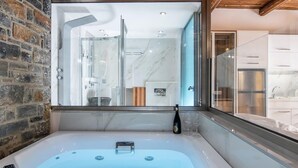 A modern bathroom with a large bathtub, a glass shower enclosure, and a view of the kitchen through a large window. - Elena Junior Deluxe Suite by Estia (Agios Vasileios)