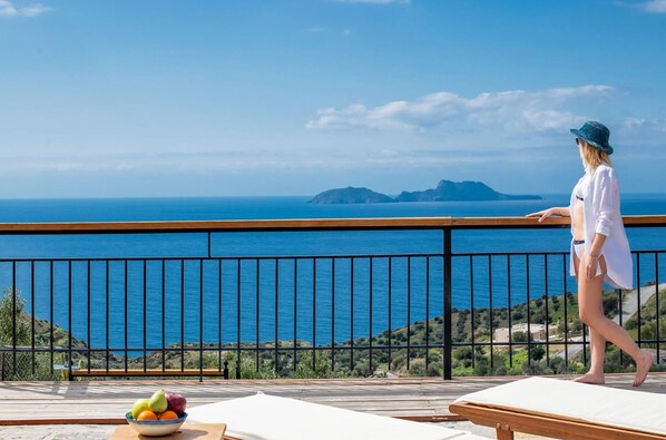 Un balcon avec vue sur la mer, un panier de fruits et une personne qui se promène.