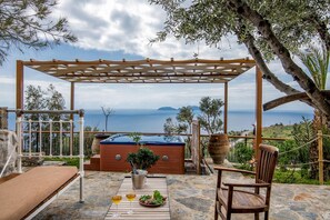 Eine Steinterrasse mit einer Holzpergola, einem Whirlpool und einem Tisch mit Getränk und Salat.