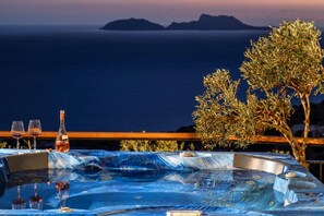 Ein Whirlpool mit Blick auf das Meer und die Berge, zwei Weingläser und eine Weinflasche.