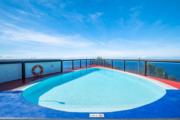 Ein Pool mit blauem Himmel im Hintergrund, umgeben von einem Glasgeländer und einem Rettungsring.