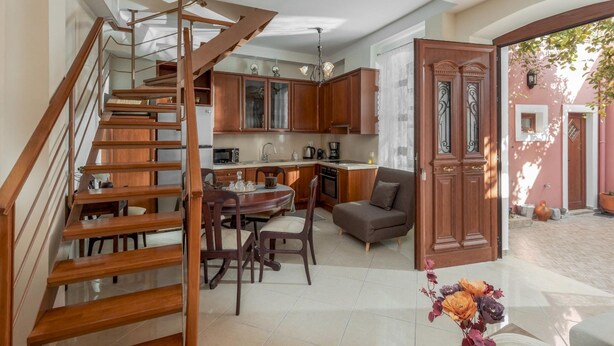 A modern kitchen with wooden cabinets, a dining area with a table and chairs, and a staircase leading to another level.