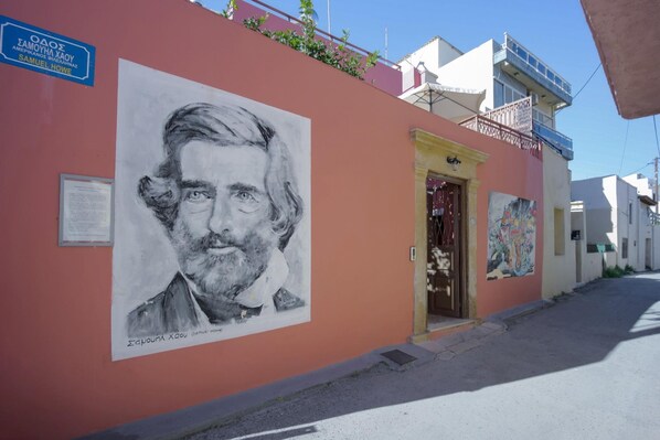 A building with a large portrait mural on the side, a signboard, and a door with a colorful artwork above it. - Palazzo Di Venus by Estia (Heraklion)