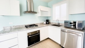 A modern kitchen with white cabinets, stainless steel appliances, a gas stove, oven, dishwasher, and a built-in microwave. - Residences C14-1d in Chame (Punta Chame)
