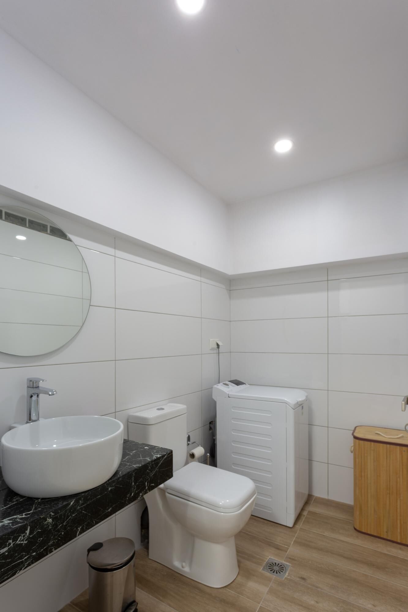 Une salle de bain moderne avec un lavabo blanc, des toilettes et un lave-linge encastré.