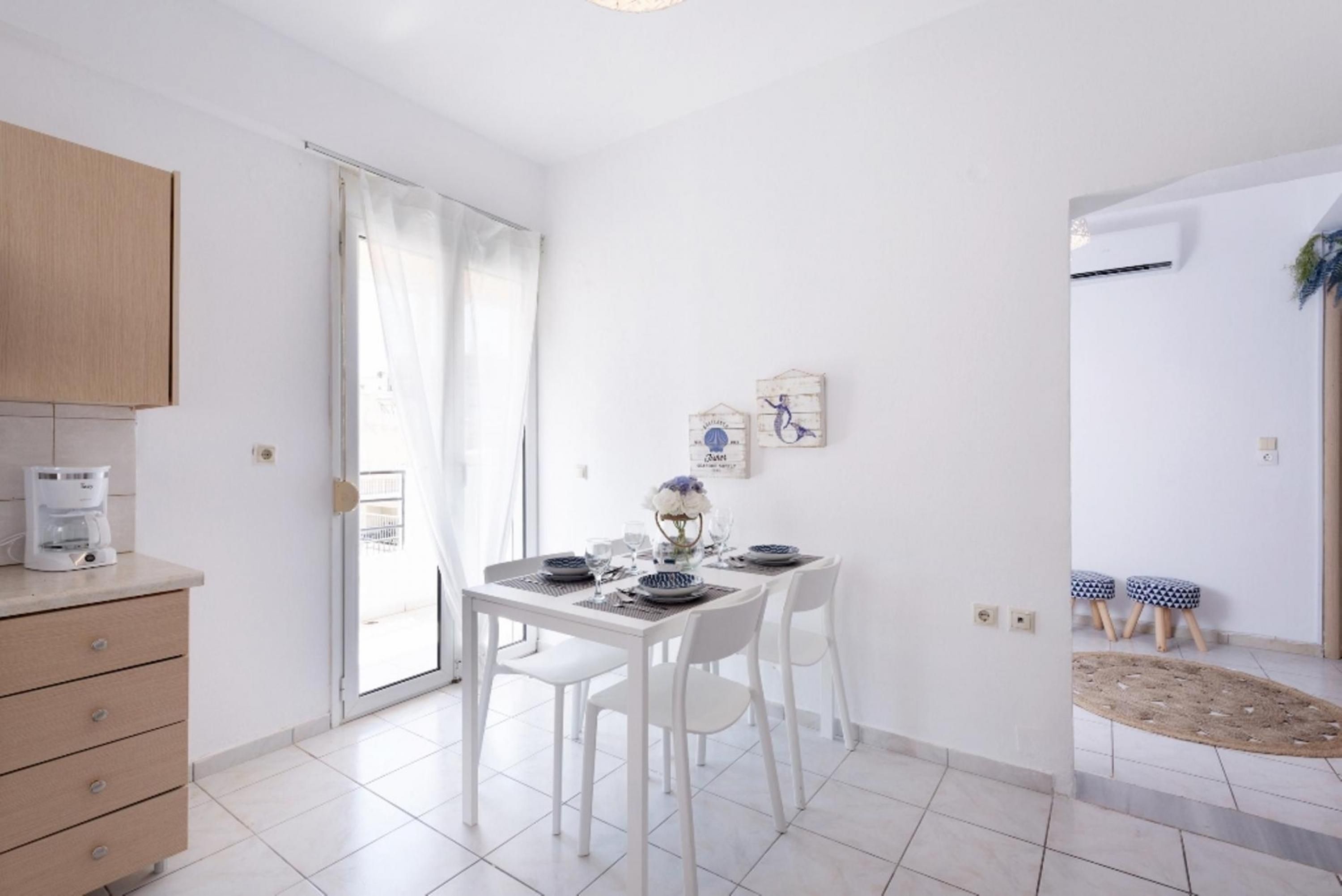 Een moderne keuken met witte kastjes, een koffiezetapparaat, en een eethoek met een witte tafel gedekt voor vier personen.