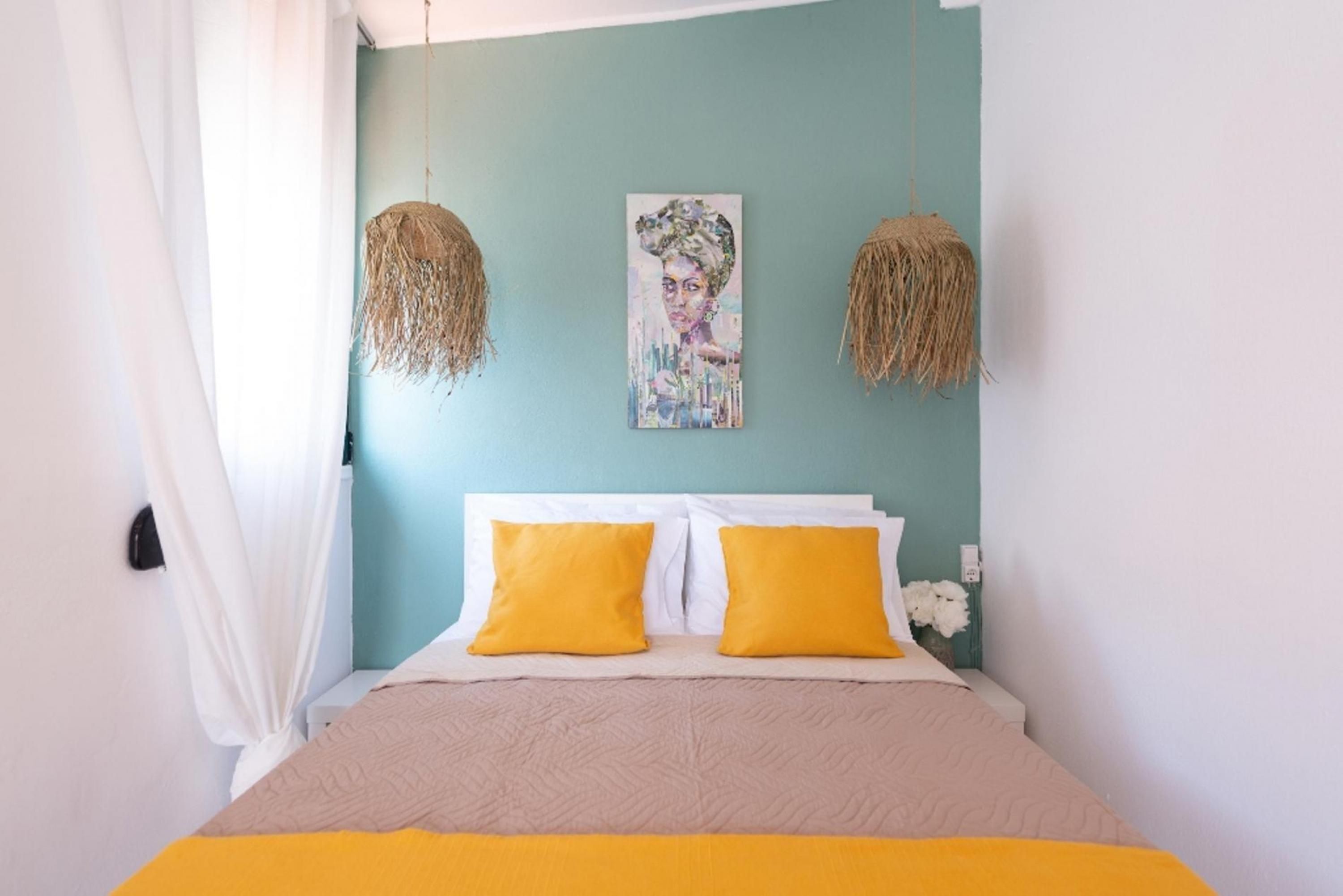 A bedroom with a bed, two yellow pillows, a teal wall, and a hanging artwork.