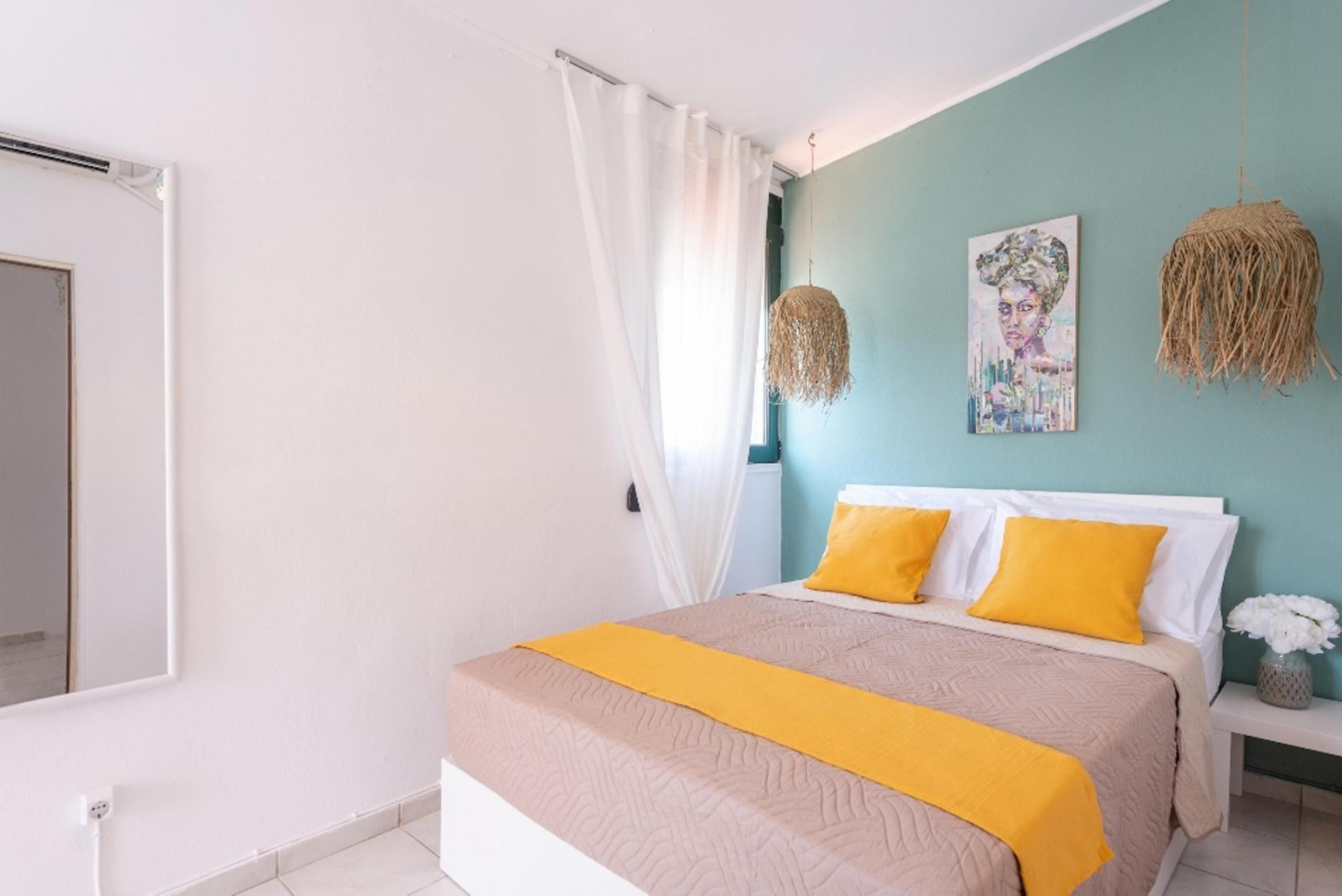 A bedroom with a bed, white curtains, a teal wall, and a painting.