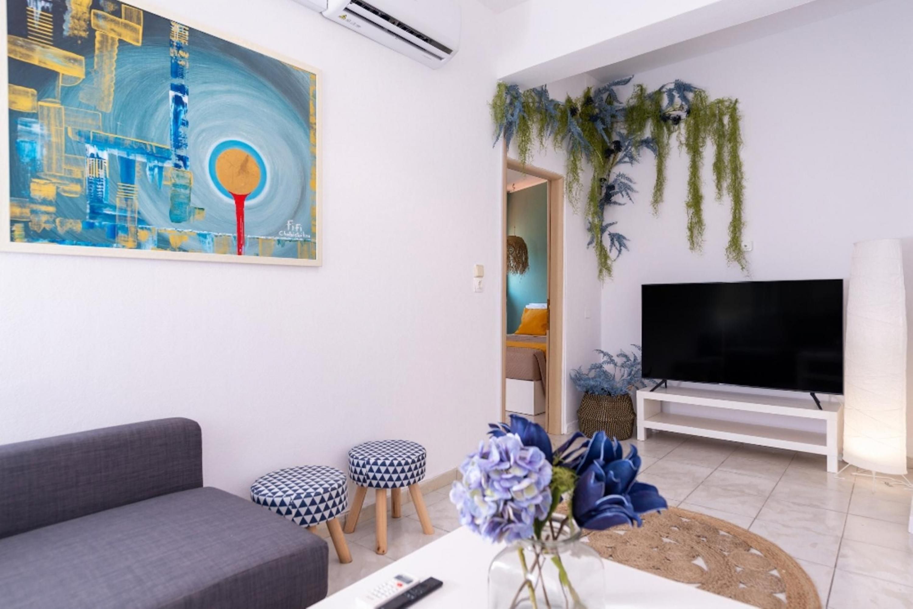 A modern living room with a grey sofa, two patterned stools, a TV, and a painting on the wall.