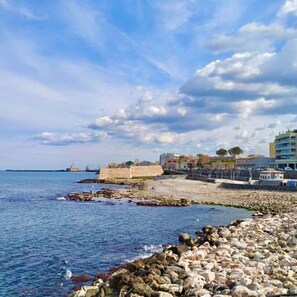 A coastal scene with a rocky shoreline, a fortified wall, and buildings in the background. - Casa Kali 1 Apartment (Heraklion)