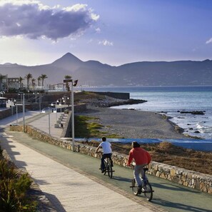 A coastal walkway with cyclists, a stone wall, and a view of the sea and mountains. - Casa Kali 1 Apartment (Heraklion)