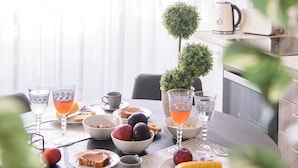 Une table de petit-déjeuner avec divers aliments, des verres de jus d’orange et une petite plante en pot.
