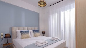 Une chambre d’hôtel moderne avec un grand lit, deux lampes de chevet, une table de chevet et une vue sur l’extérieur à travers des rideaux légers.