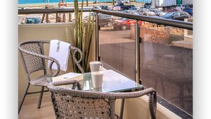 Un balcon avec des fauteuils en osier, une table et une vue sur la plage et les voitures garées.