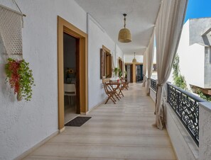 A corridor with a wooden floor, a dining area with chairs and a table, and a hanging plant.