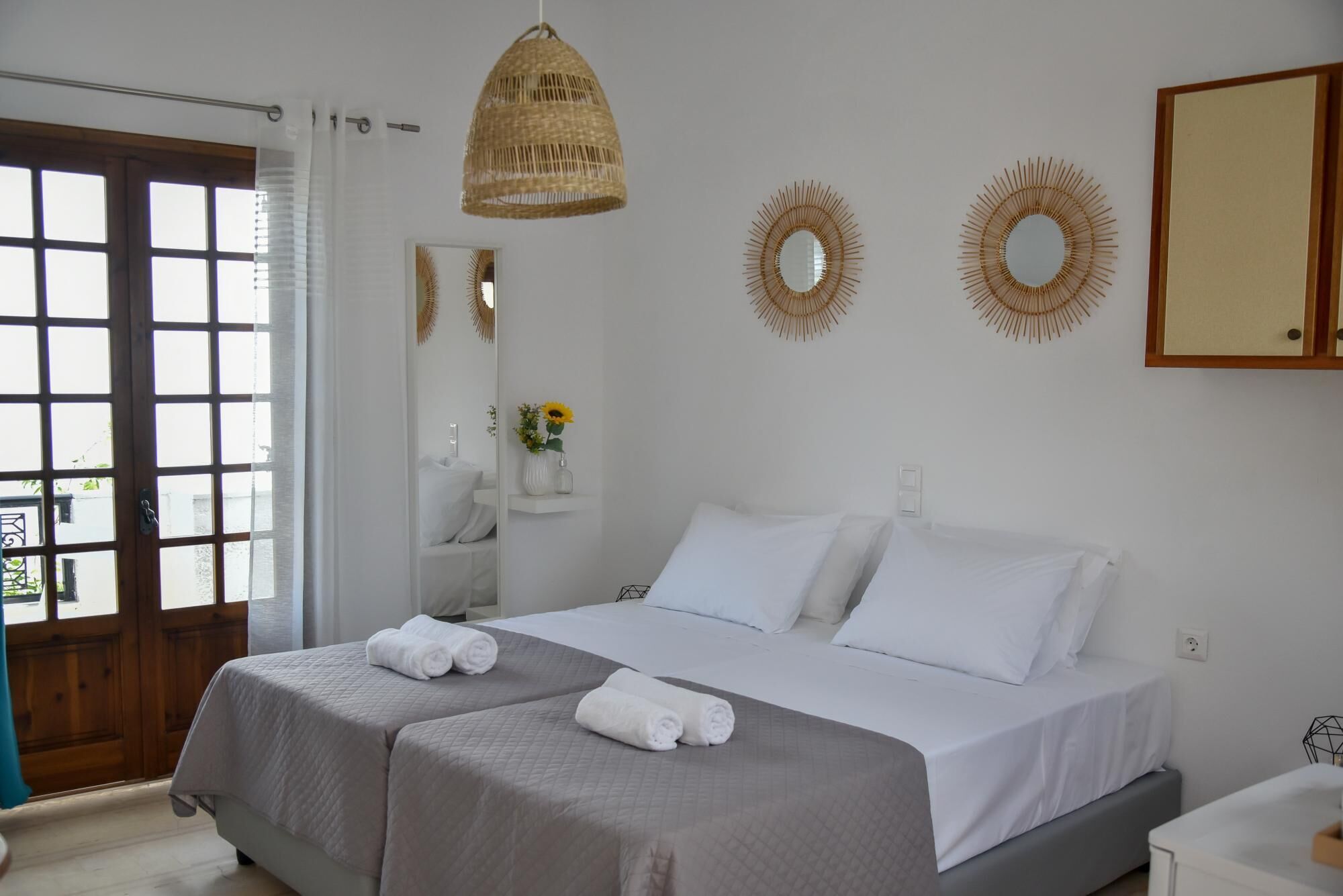 A hotel room with two beds, a large mirror, decorative wall mirrors, and a wicker pendant light.