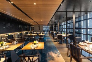 A modern dining area with tables and chairs, a long counter, and a large window providing natural light.