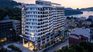 Un hôtel à plusieurs étages, doté d’une architecture moderne et de balcons à chaque niveau, situé à proximité d’un plan d’eau.