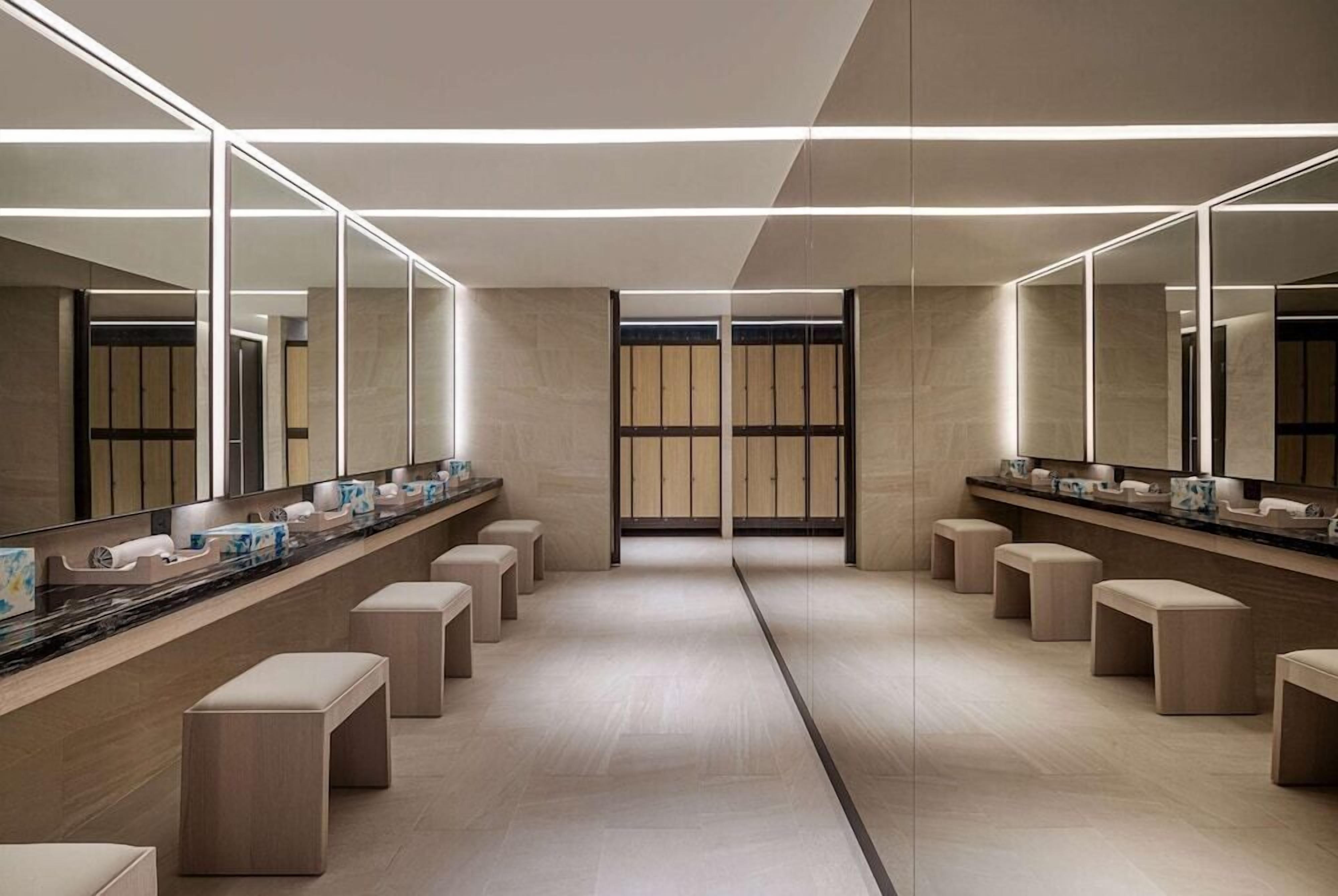 A modern restroom with mirrored walls, a long counter, and multiple stools.