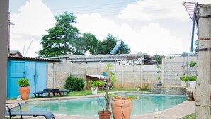 Ein Garten mit Swimmingpool, einer blauen Tür und einer kleinen Terrasse mit Tisch und Stühlen.