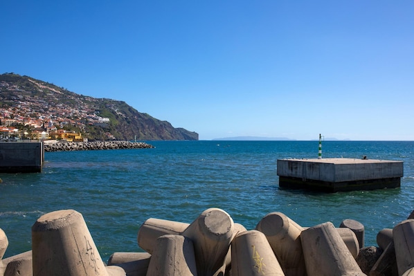A coastal scene with a pier, a lighthouse, and a hillside town.