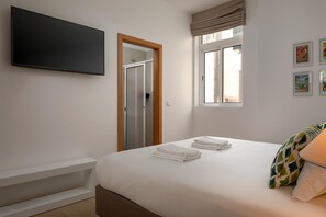 A bedroom with a bed, a TV mounted on the wall, a window with curtains, and a door.