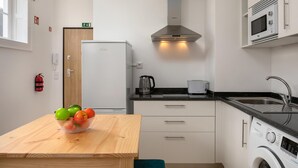 Una cocina moderna con una mesa de madera, un frutero, una lavadora y un microondas.