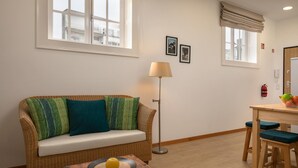 Una habitación amoblada con un sofá, una mesa con un frutero, una lámpara de pie y un comedor con sillas.