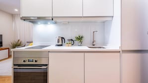 Una cocina moderna con armarios blancos, una campana extractora de acero inoxidable, una tetera y una pequeña planta en la encimera.