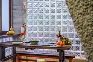 A dining table set with plates, glasses, and a bottle of wine, with a window in the background. - King Shelter by Homie (Porto Moniz)