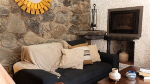 A cozy living room with a stone wall, a dark sofa, a wooden coffee table, and a fireplace. - King Shelter by Homie (Porto Moniz)