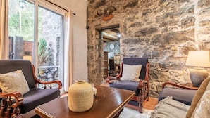 A cozy room with stone walls, a large window, and a wooden table with a vase. - King Shelter by Homie (Porto Moniz)